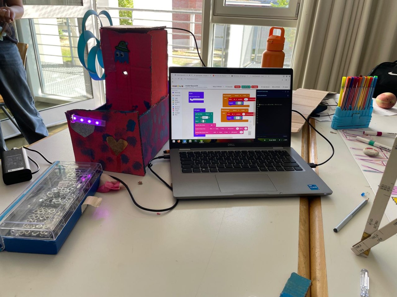 Live-Action: Code am Laptop, lila LEDs und kreativer Karton-Bau.